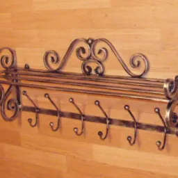 Kuty, metalowy wieszak na ubrania z półką, zdobiony ornamentami w stylu retro, zamontowany na drewnianej ścianie.