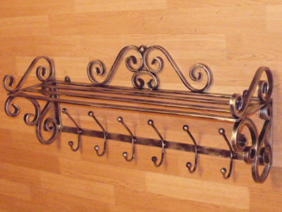 Kuty, metalowy wieszak na ubrania z półką, zdobiony ornamentami w stylu retro, zamontowany na drewnianej ścianie.