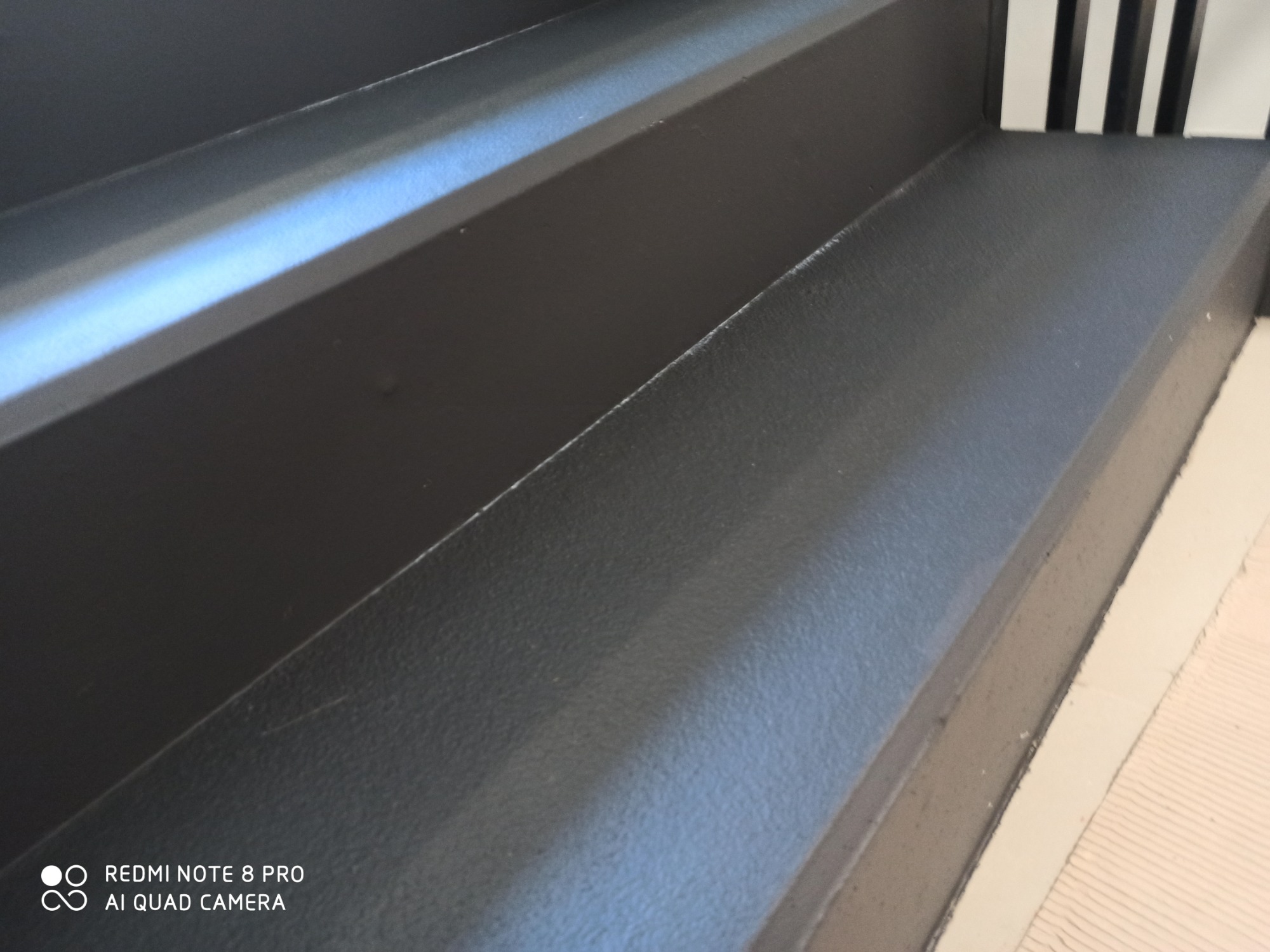 Czarne schody z wykończeniem żywicznym, widoczne z bliska, z fragmentem białych pionowych desek w tle.