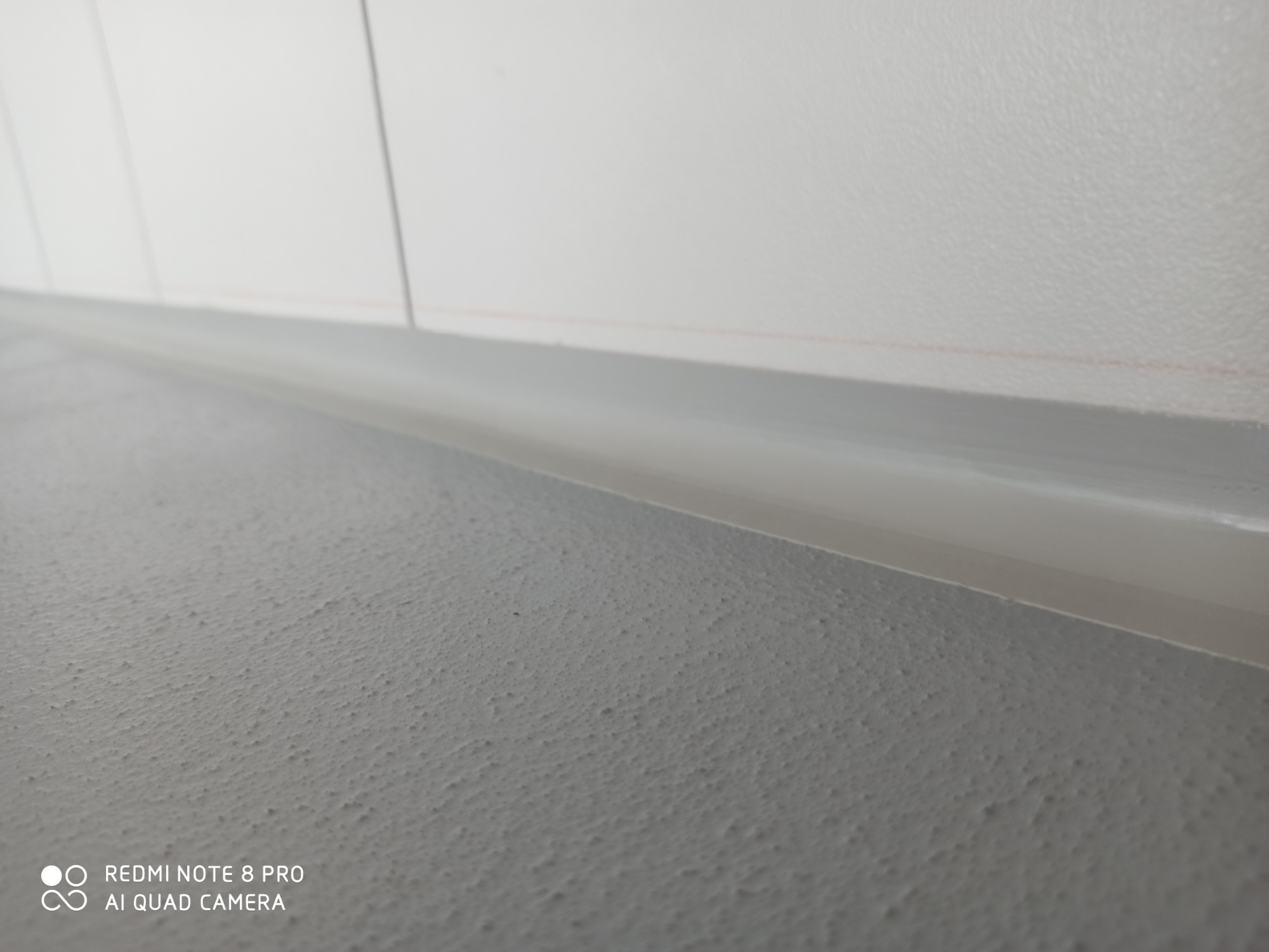 Szara, chropowata powierzchnia podłogi z widocznym, szarym cokołem przy białej ścianie.