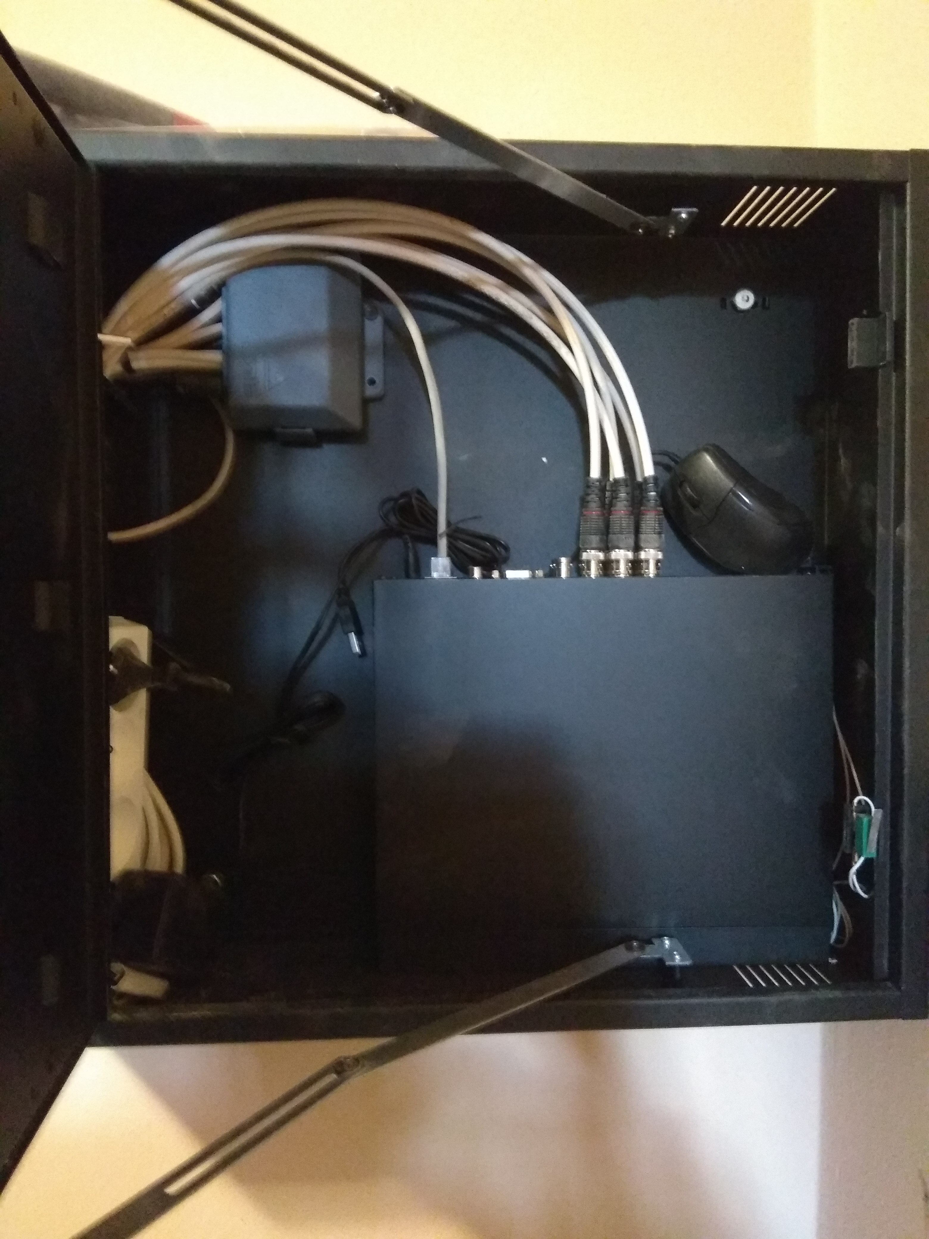 Zamknięta czarna szafka z przewodami i rejestratorem systemu monitoringu w Kłodzku, widoczna myszka komputerowa.