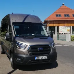 Szary Ford Transit na przejściu dla pieszych przed Zajazdem Głowaczówka w słoneczny dzień.