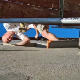 Pracownik w koszulce z logo Weber wygładza świeżo nałożony tynk na elewacji budynku za pomocą pędzla, stojąc na rusztowaniu.