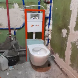 Montaż podwieszanej miski WC z widocznym stelażem KK POL, instalacją wodną z rur PEX w kolorach czerwonym i niebieskim oraz surowymi ścianami w trakcie remontu.