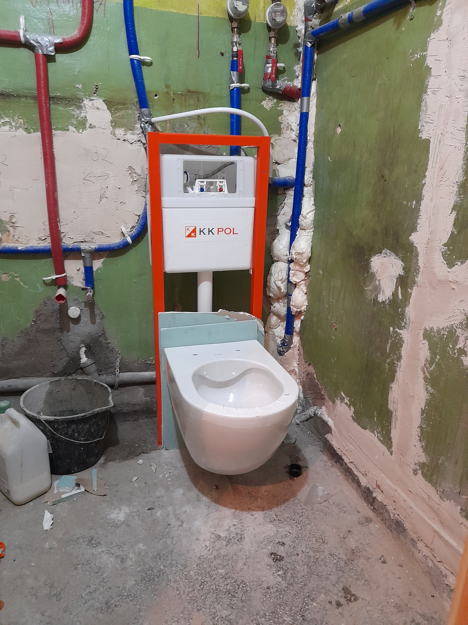 Montaż podwieszanej miski WC z widocznym stelażem KK POL, instalacją wodną z rur PEX w kolorach czerwonym i niebieskim oraz surowymi ścianami w trakcie remontu.