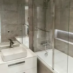 Nowoczesna łazienka z umywalką nablatową, szklaną kabiną prysznicową i szarymi płytkami imitującymi kamień, oświetlenie LED w niszy.