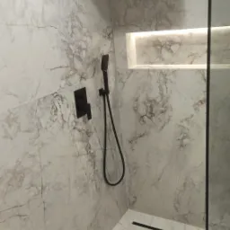 Nowoczesna kabina prysznicowa z marmurowymi płytkami, czarną armaturą i liniowym odpływem.