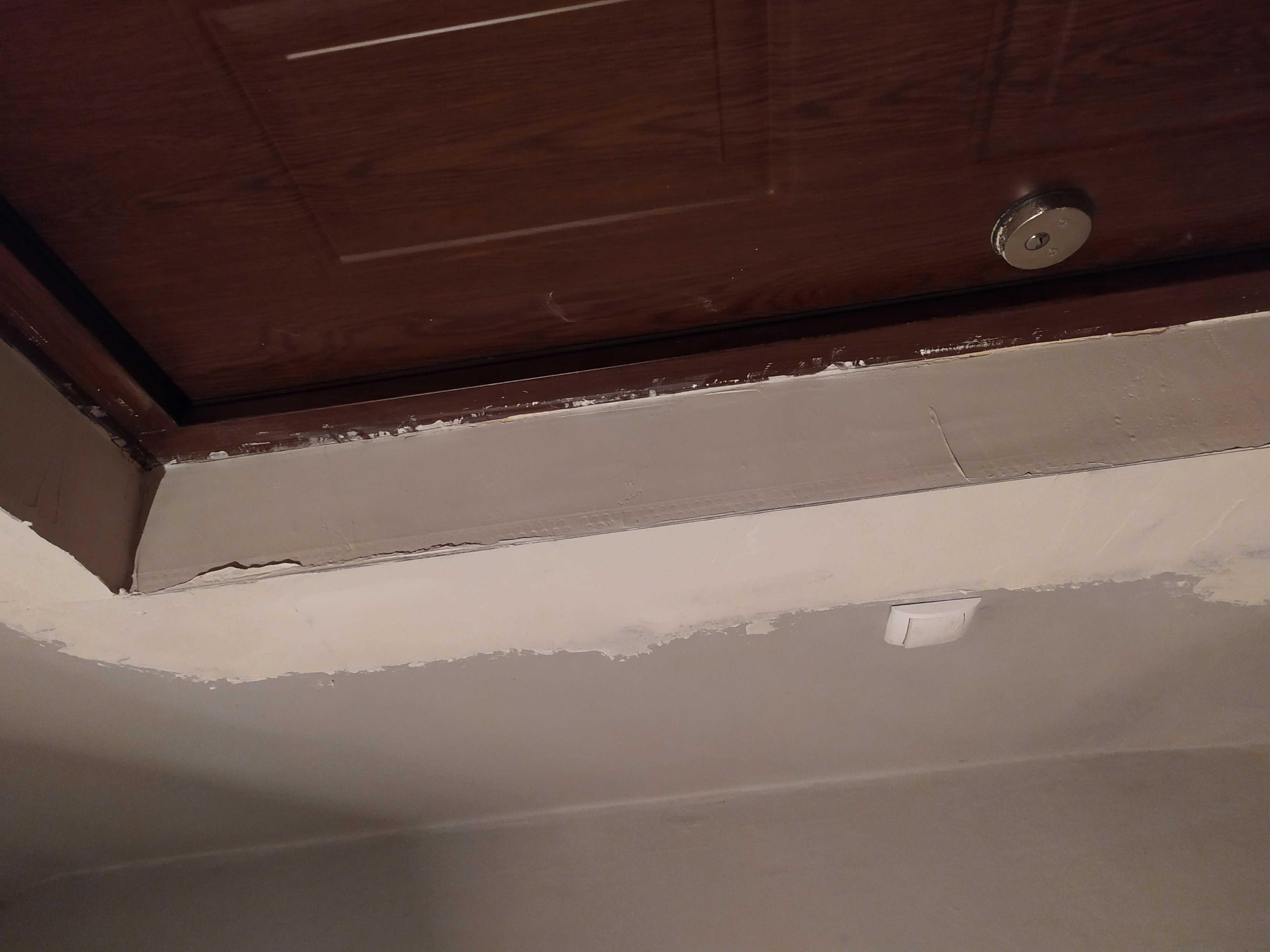 Niedokończone połączenie ściany z sufitem, widoczne ślady po szpachlowaniu, nierówności i taśma malarska przy drewnianych drzwiach.