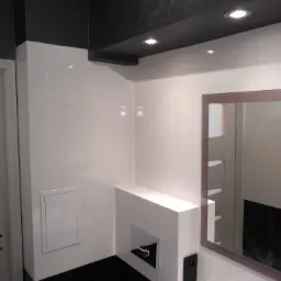 Nowoczesna łazienka z białymi płytkami, czarnym sufitem z oświetleniem punktowym i dużym lustrem z brązową ramą, widoczny fragment umywalki z baterią.