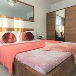 OREST - Nowoczesna sypialnia z drewnianym łóżkiem, koralową narzutą i okrągłymi poduszkami. Duże lustro na ścianie odbija schody. Przesuwne drzwi szafy z lustrzanymi panelami.