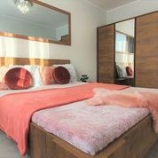 Nowoczesna sypialnia z drewnianym łóżkiem, koralową narzutą i okrągłymi poduszkami. Duże lustro na ścianie odbija schody. Przesuwne drzwi szafy z lustrzanymi panelami.