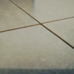 Beżowe płytki podłogowe z brązową fugą, ułożone równo, sfotografowane z niskiej perspektywy.