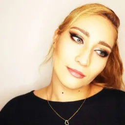 Portret kobiety z profesjonalnym, wieczorowym smoky eye, delikatnym konturowaniem i błyszczącymi ustami, patrzącej w bok, z widocznym złotym naszyjnikiem z zawieszką w kształcie serca.