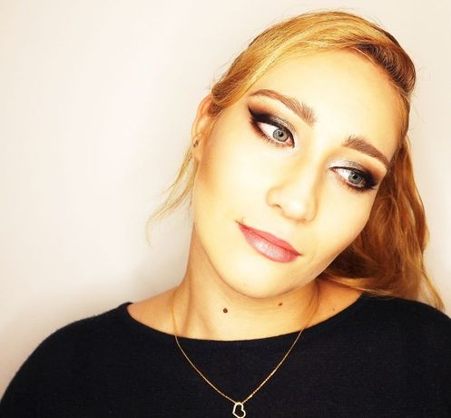 Portret kobiety z profesjonalnym, wieczorowym smoky eye, delikatnym konturowaniem i błyszczącymi ustami, patrzącej w bok, z widocznym złotym naszyjnikiem z zawieszką w kształcie serca.