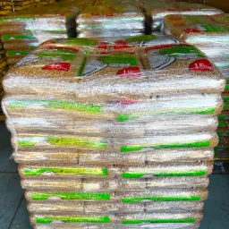 Stos palet z workami pelletu drzewnego, owinięty folią stretch, widoczne etykiety z napisem 15kg i logo producenta, w tle składowane elementy drewniane.