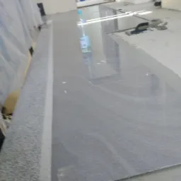 Szare, matowe płytki podłogowe ułożone w pomieszczeniu w trakcie prac wykończeniowych, widoczna butelka wody i narzędzia na powierzchni płytek.