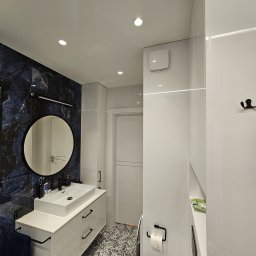 Flormeb - Nowoczesna łazienka z umywalką nablatową na szafce z szufladami, okrągłym lustrem w czarnej ramie na ścianie z efektem ciemnego marmuru, wzorzystą podłogą i białymi ścianami z wbudowanymi szafkami.