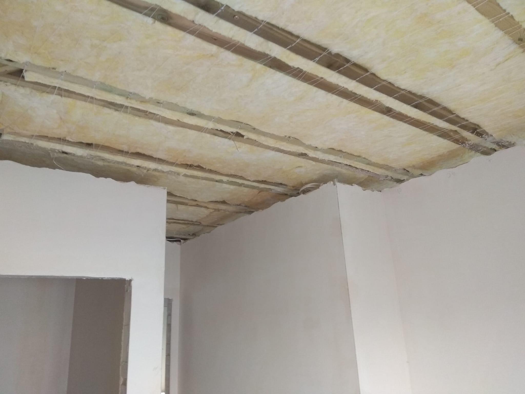 Poddasze z widoczną izolacją termiczną między drewnianymi belkami, zabezpieczoną siatką przed dalszymi pracami wykończeniowymi.