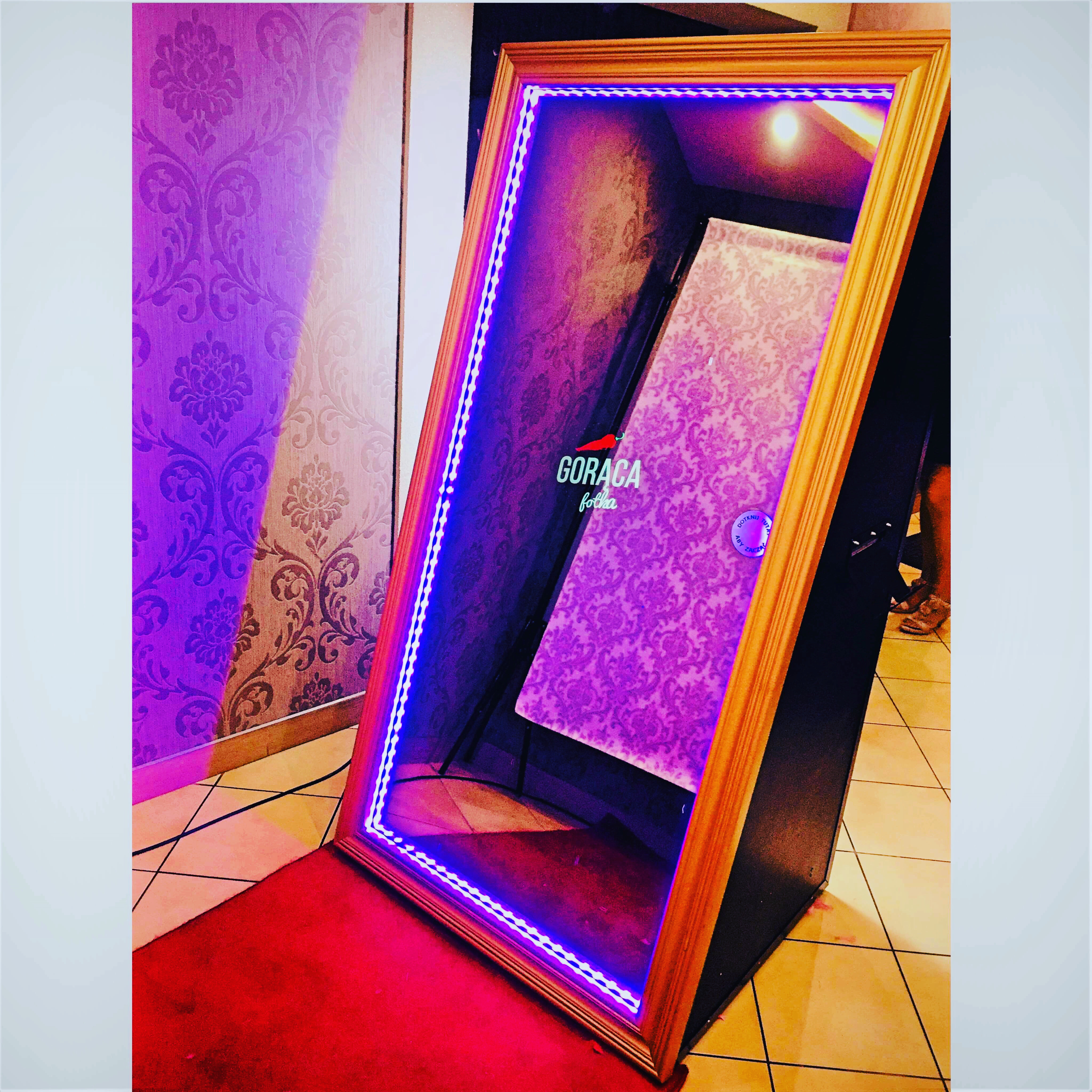 Ustawiona fotobudka w formie lustra z oświetleniem LED na czerwonym dywanie, widoczne wzorzyste tło.