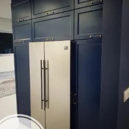 Granatowe szafki kuchenne na wymiar z lodówką w zabudowie, złote uchwyty, widok z dołu.