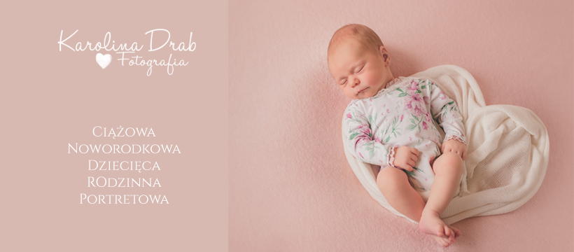 Śpiące niemowlę w kwiecistym body, ułożone w sercowatym otulaczu na różowym tle.