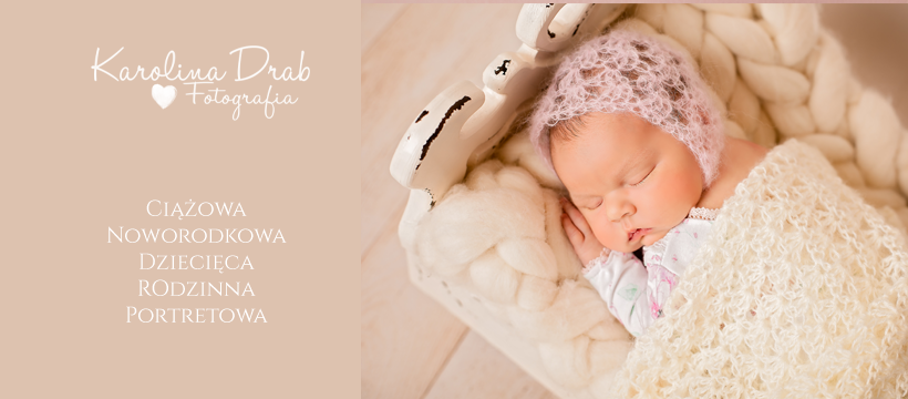 Śpiące nowonarodzone dziecko w ażurowej czapeczce, otulone kremowym kocem w białym, stylizowanym koszu z grubych włóczek.