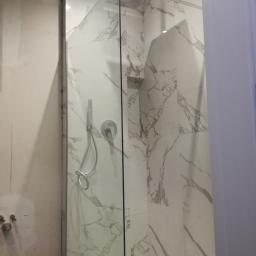 Tomek - Nowoczesna kabina prysznicowa z deszczownicą i baterią podtynkową na ścianie wyłożonej białymi płytkami imitującymi marmur, widok na ścianę w trakcie prac wykończeniowych.