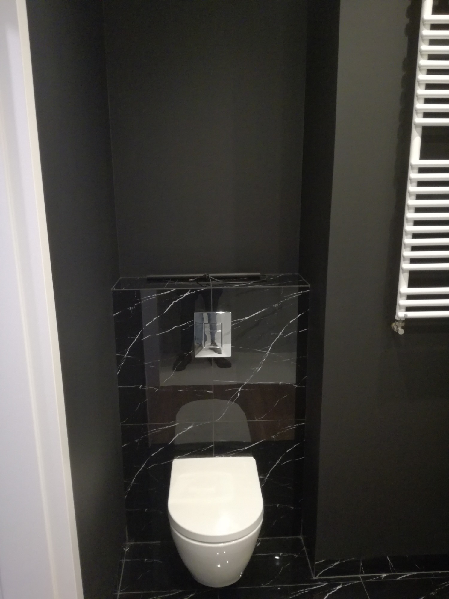 Nowoczesna toaleta podwieszana w czarnej łazience z płytkami imitującymi marmur i grzejnikiem drabinkowym.
