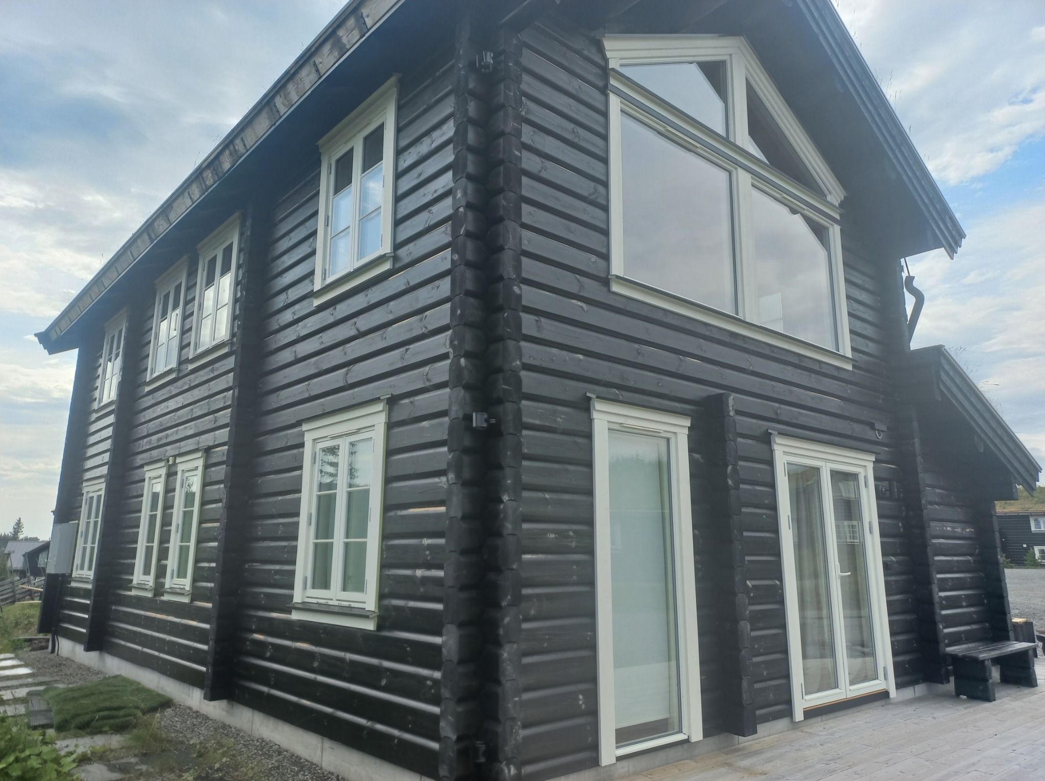 Ciemna, drewniana elewacja domu z jasnymi ramami okiennymi i dużym oknem trójkątnym na poddaszu, widok z dołu.