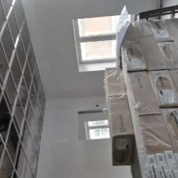 Metalowa konstrukcja szkieletowa ściany z płyt kartonowo-gipsowych, widok od dołu, obok stos zapakowanych płyt Rockfon, okna w tle.