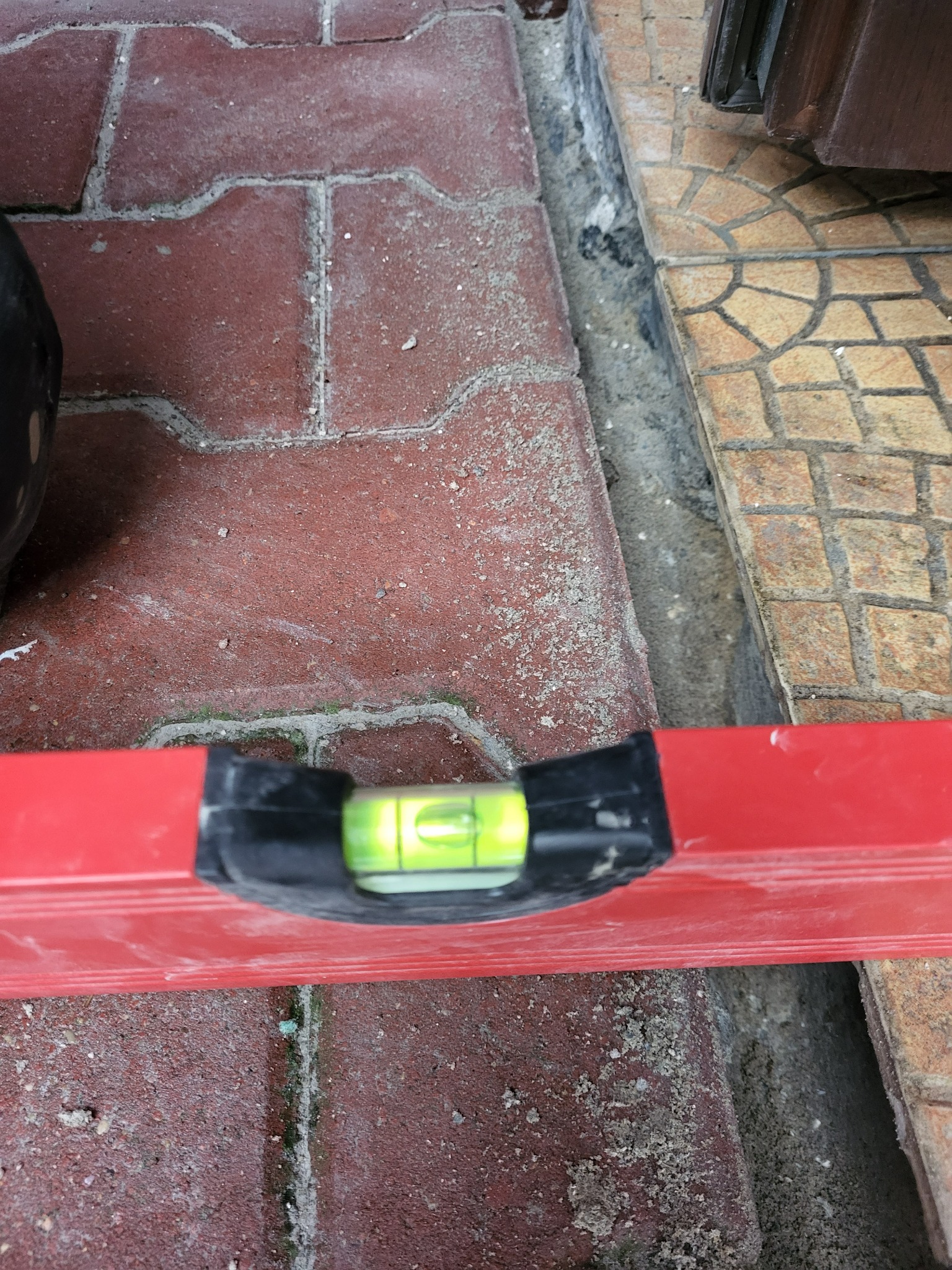 Czerwony poziomica na kostce brukowej, sprawdzanie poziomu. Fragment mozaiki w tle. Detal z prac wykończeniowych.