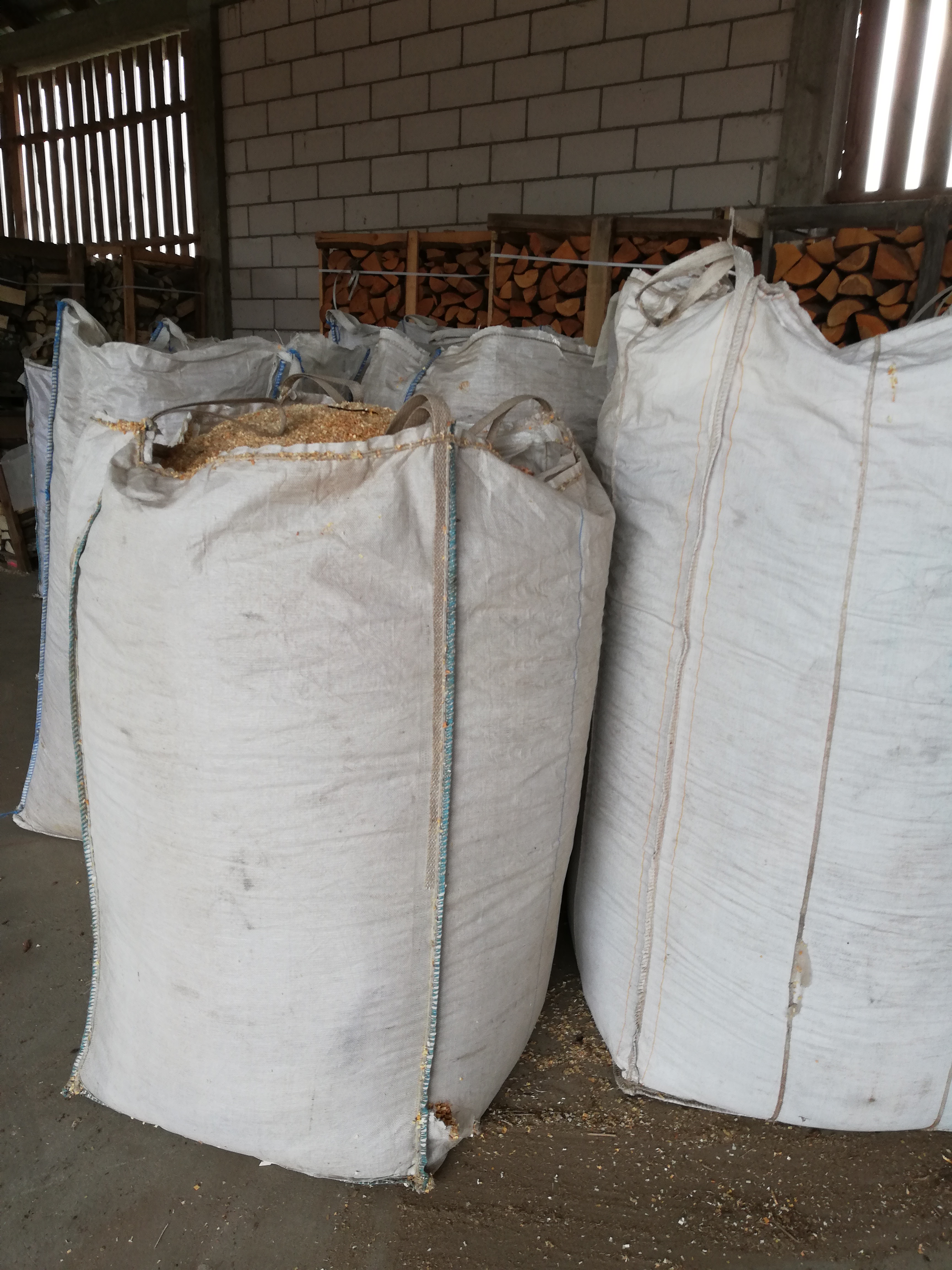 Duże, białe worki wypełnione pociętym drewnem, składowane w magazynie w Janowie. W tle widoczne ułożone szczapy drewna.