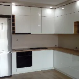 Nowoczesna, biała kuchnia z drewnianym blatem, zrealizowana w Krakowie. Widoczna lodówka w zabudowie, płyta indukcyjna i piekarnik w czarnym kolorze.