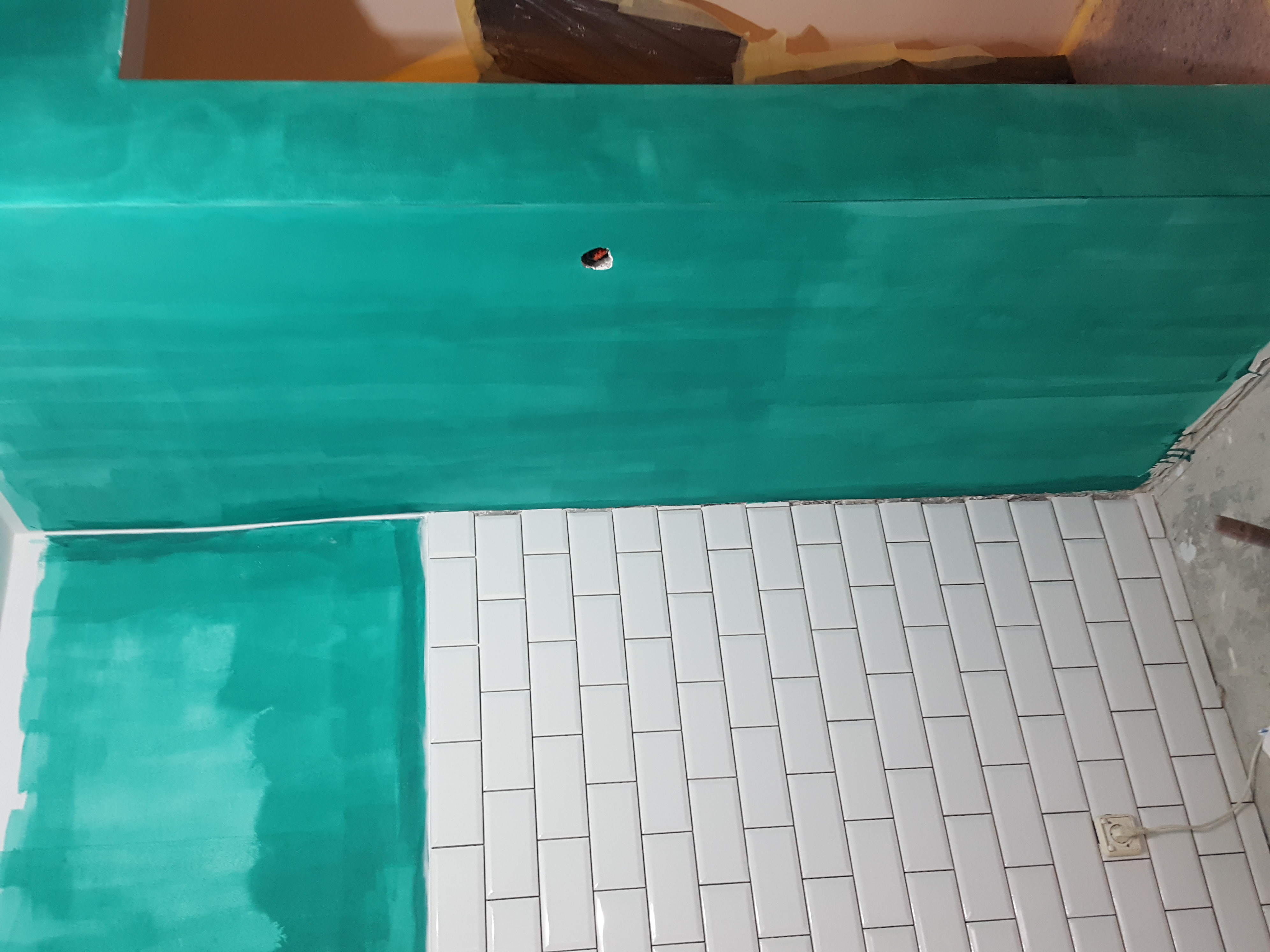 Świeżo pomalowany na turkusowo sufit i fragment ściany nad białymi, podłużnymi płytkami na ścianie, widoczna puszka elektryczna w suficie.