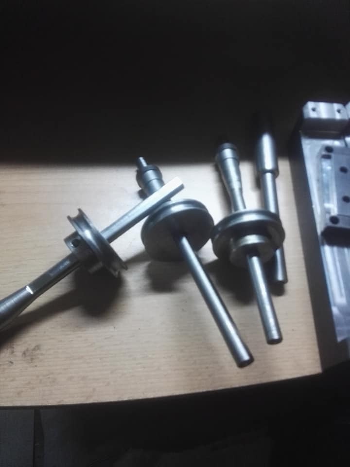 Metalowe elementy obrobione na tokarce, widoczne ślady obróbki, ułożone na drewnianym blacie w słabym oświetleniu.