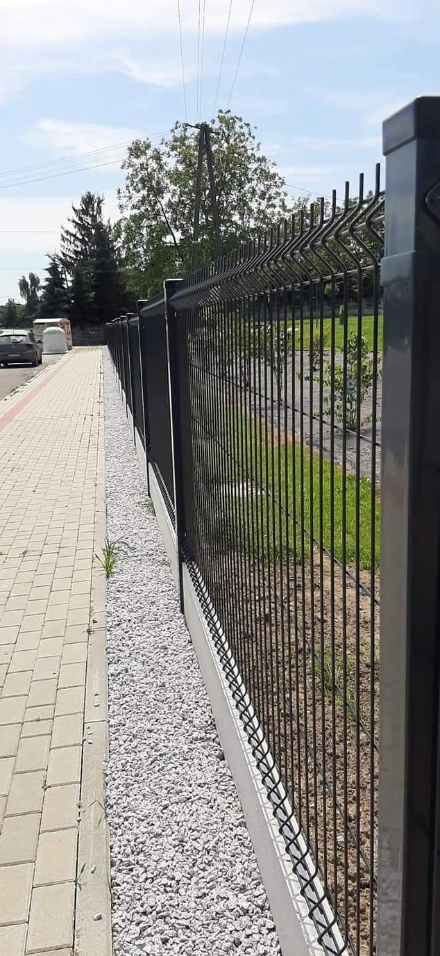 Nowoczesne ogrodzenie panelowe z podmurówką betonową i wysypanym grysem, widok z perspektywy chodnika.