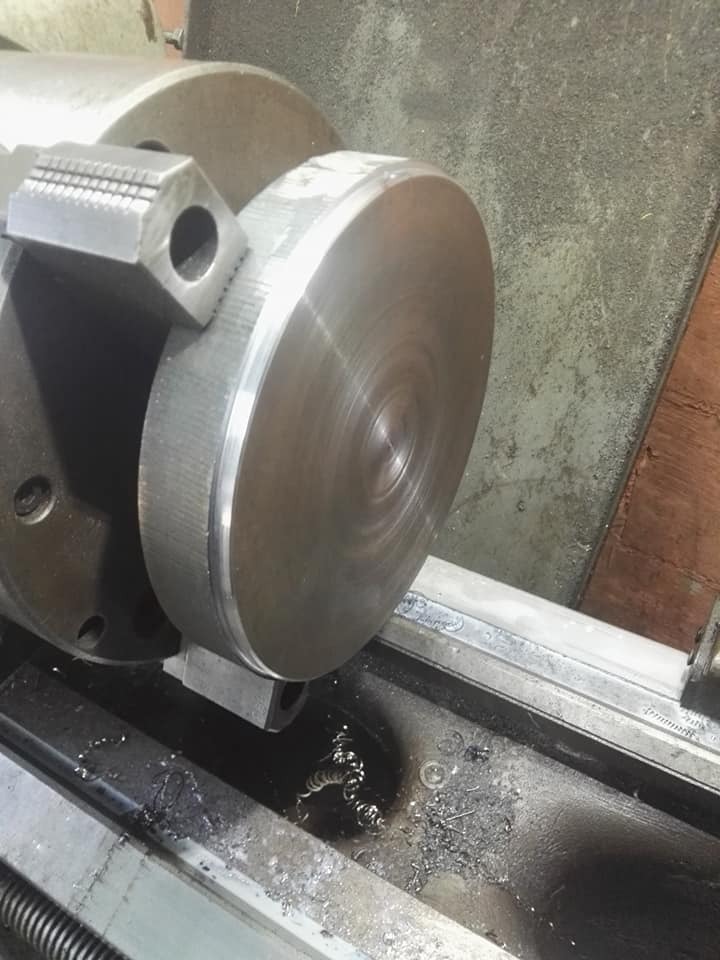 Metalowy element obrabiany na tokarce, widoczne wióry i uchwyt tokarski.