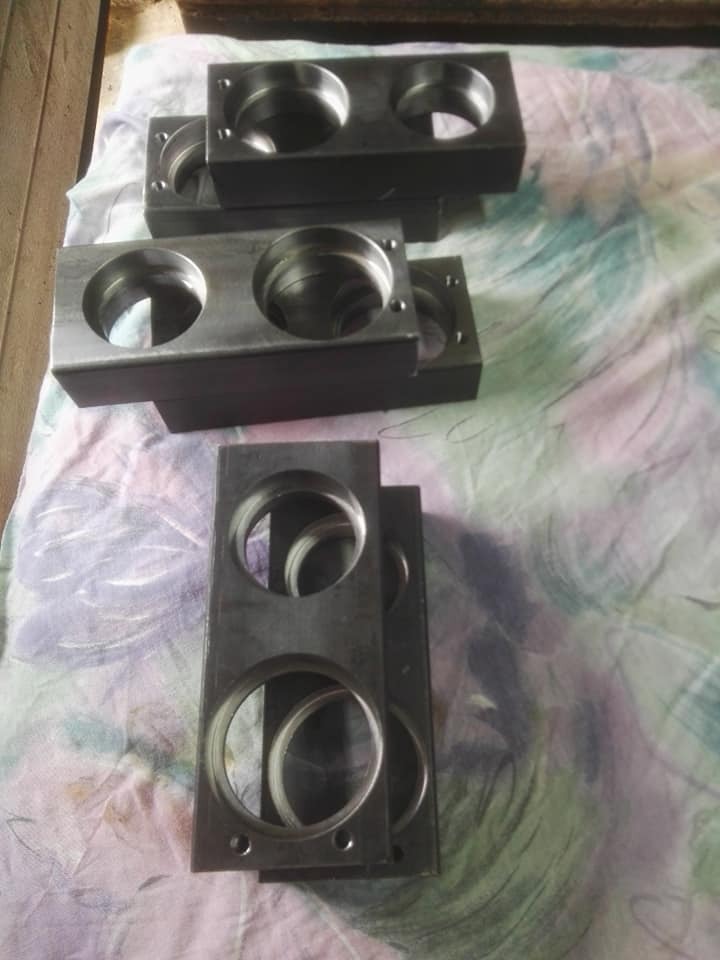 Surowe, obrobione metalowe bloki z okrągłymi otworami ułożone na wzorzystej tkaninie, widoczne ślady obróbki.