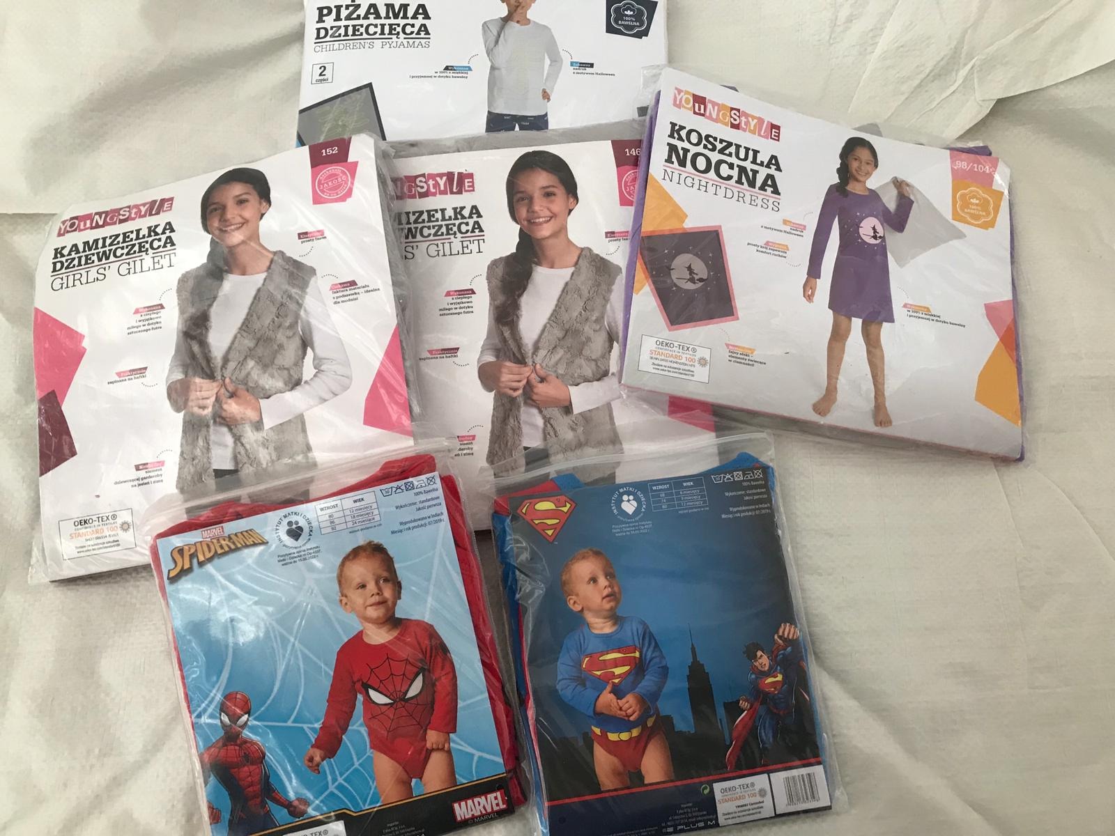 Zestaw zapakowanej odzieży dziecięcej, w tym kamizelki dziewczęce, piżamy, koszule nocne i kostiumy Spider-Mana i Supermana, ułożone na białym tle.