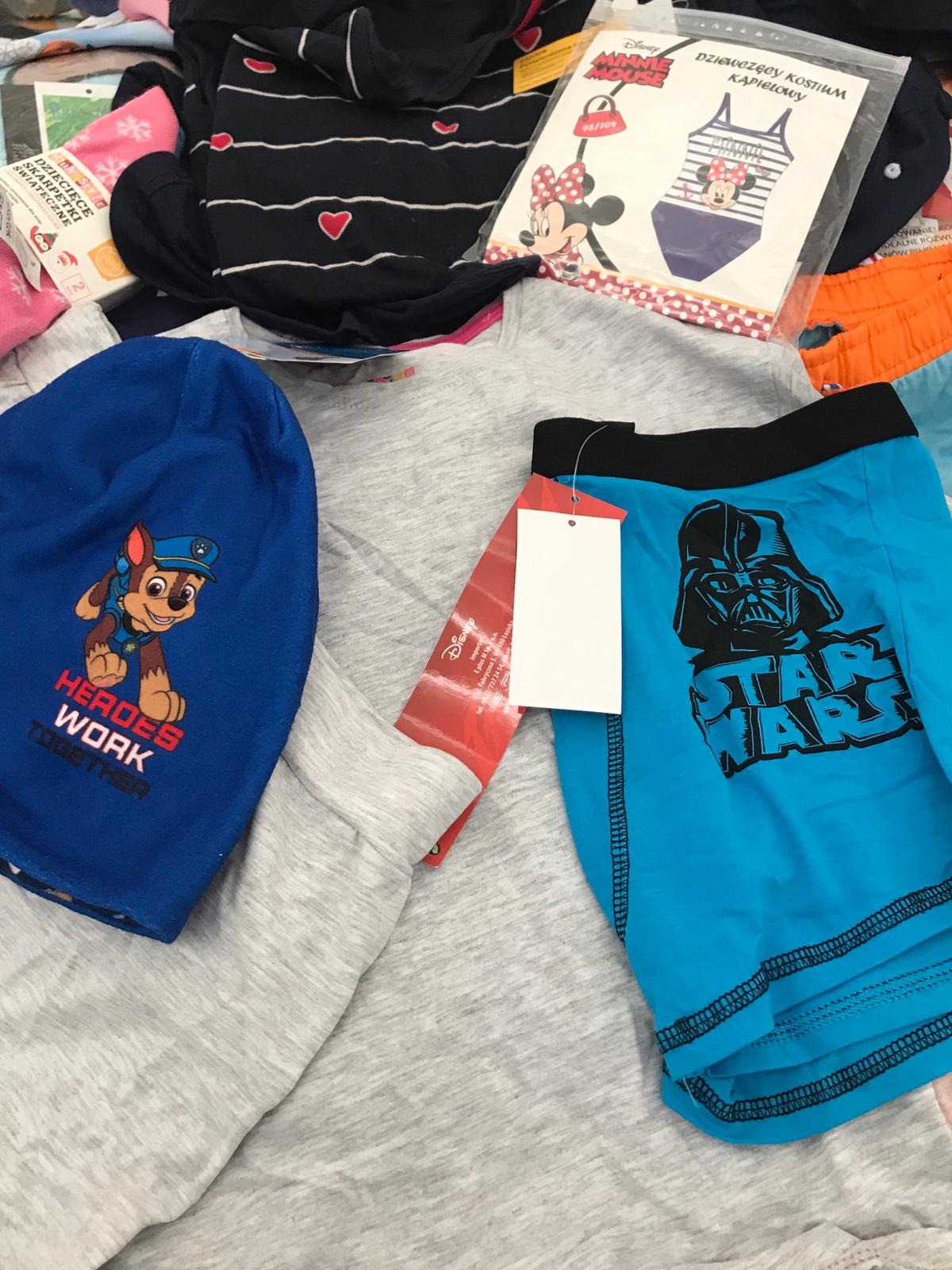 Stos ubrań dziecięcych z motywami z bajek i filmów, w tym niebieska czapka z psem Chase z Psiego Patrolu, błękitne bokserki z Darthem Vaderem ze Star Wars, piżama w paski z serduszkami i kostium...