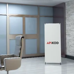 Wnętrze biura z nowoczesnym krzesłem, stołem z mikrofonami oraz banerem reklamowym z logo 'APIKOD' na tle ściany z cegły i dużego ekranu.