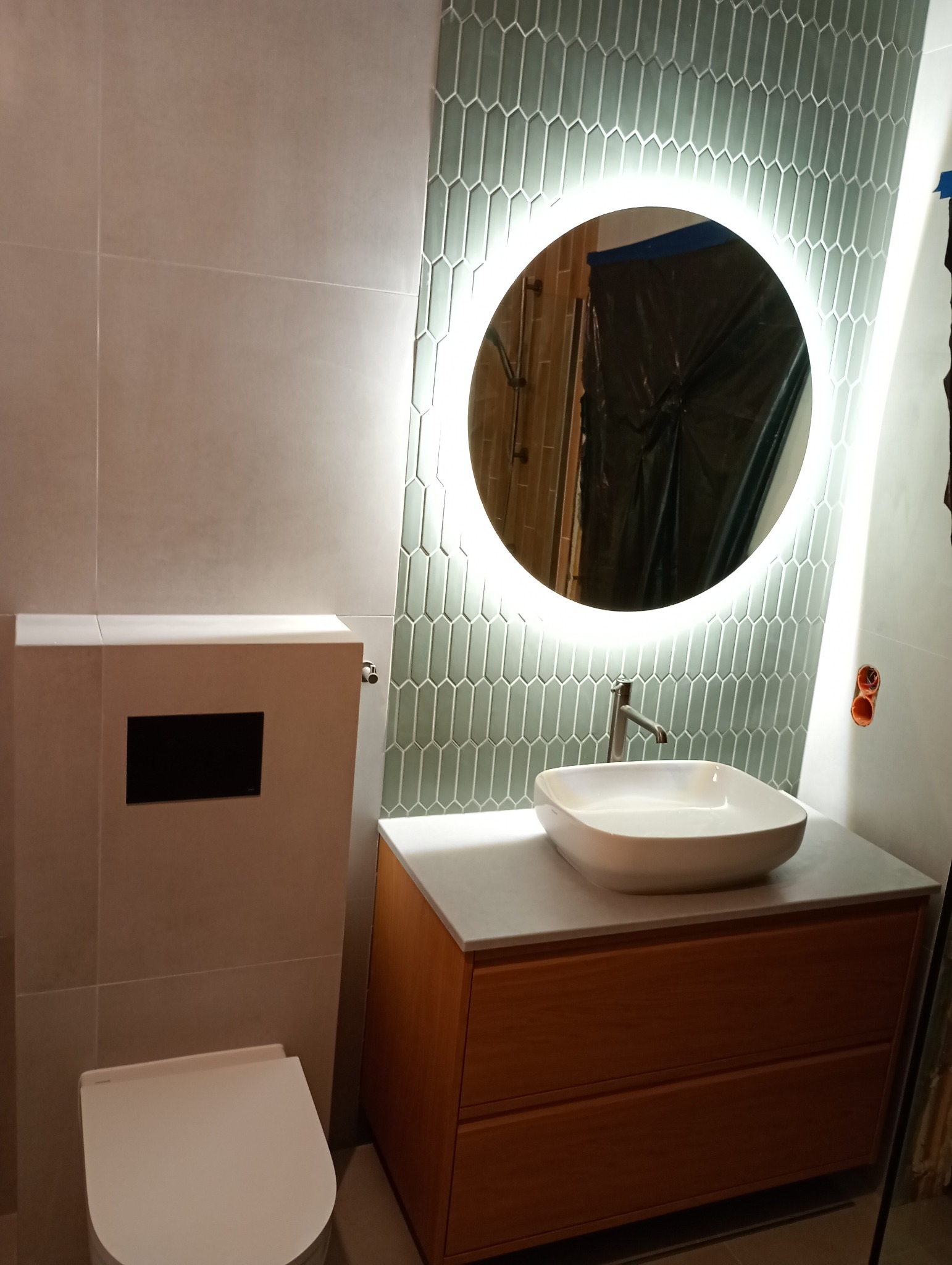 Nowoczesna łazienka z umywalką nablatową, podświetlanym lustrem i geometrycznymi płytkami w odcieniach szarości. Uwagę zwraca drewniana szafka pod umywalką.