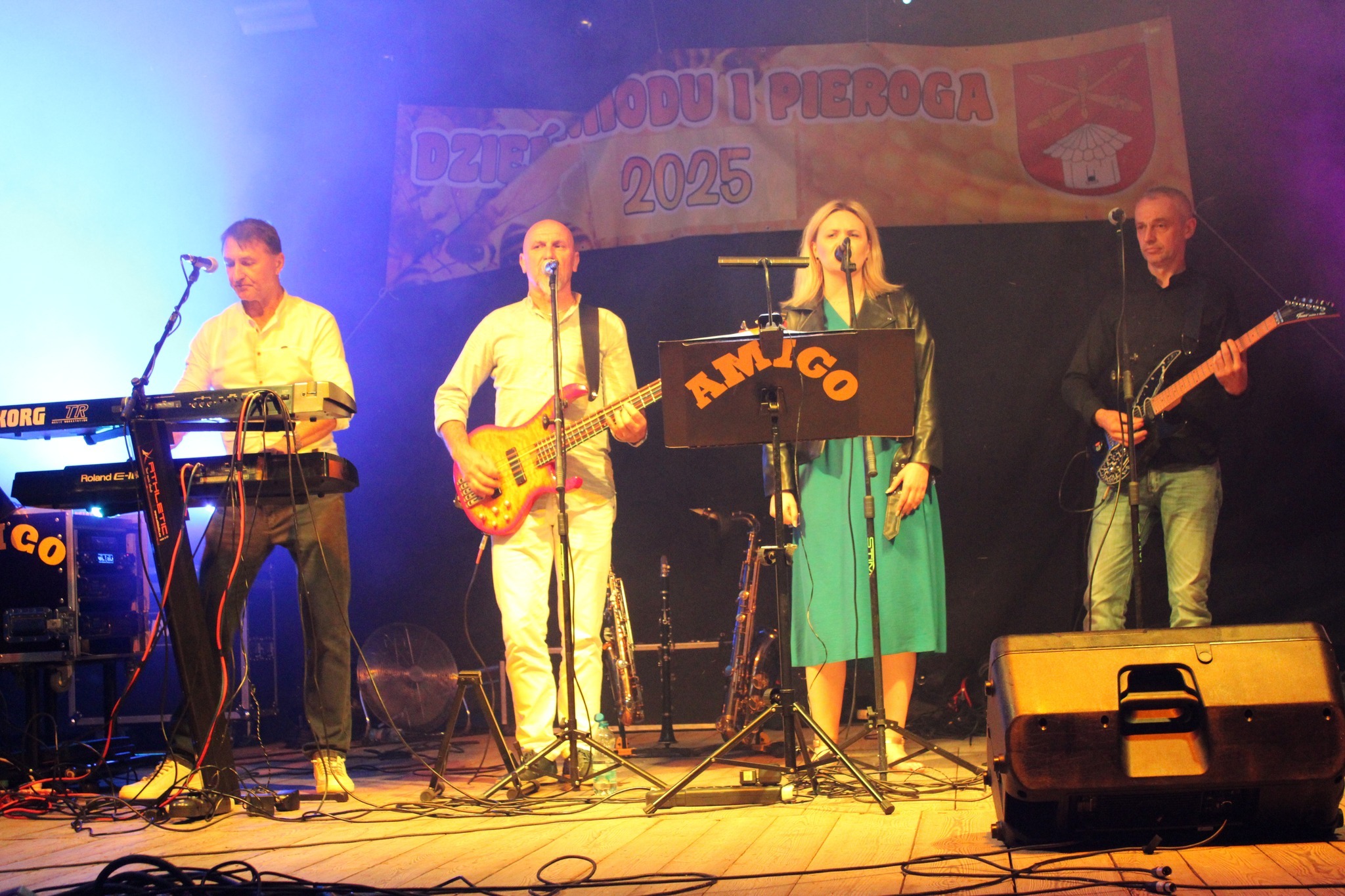 Zespół muzyczny 'Amigo' podczas występu na scenie. Czterech muzyków gra na instrumentach: klawiszach, gitarze basowej, gitarze elektrycznej i śpiewa do mikrofonu.