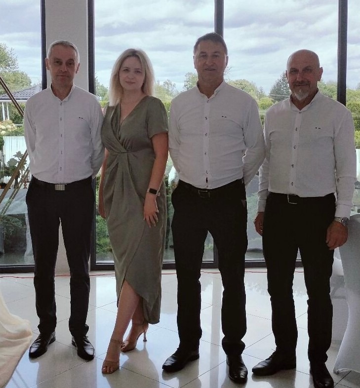 Zespół muzyczny, trzech mężczyzn w białych koszulach i czarnych spodniach oraz kobieta w sukience na tle okna podczas uroczystości.