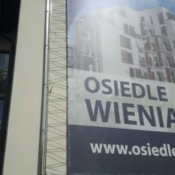 Baner reklamowy z konstrukcją nośną, prezentujący wizualizację osiedla mieszkaniowego na elewacji budynku.