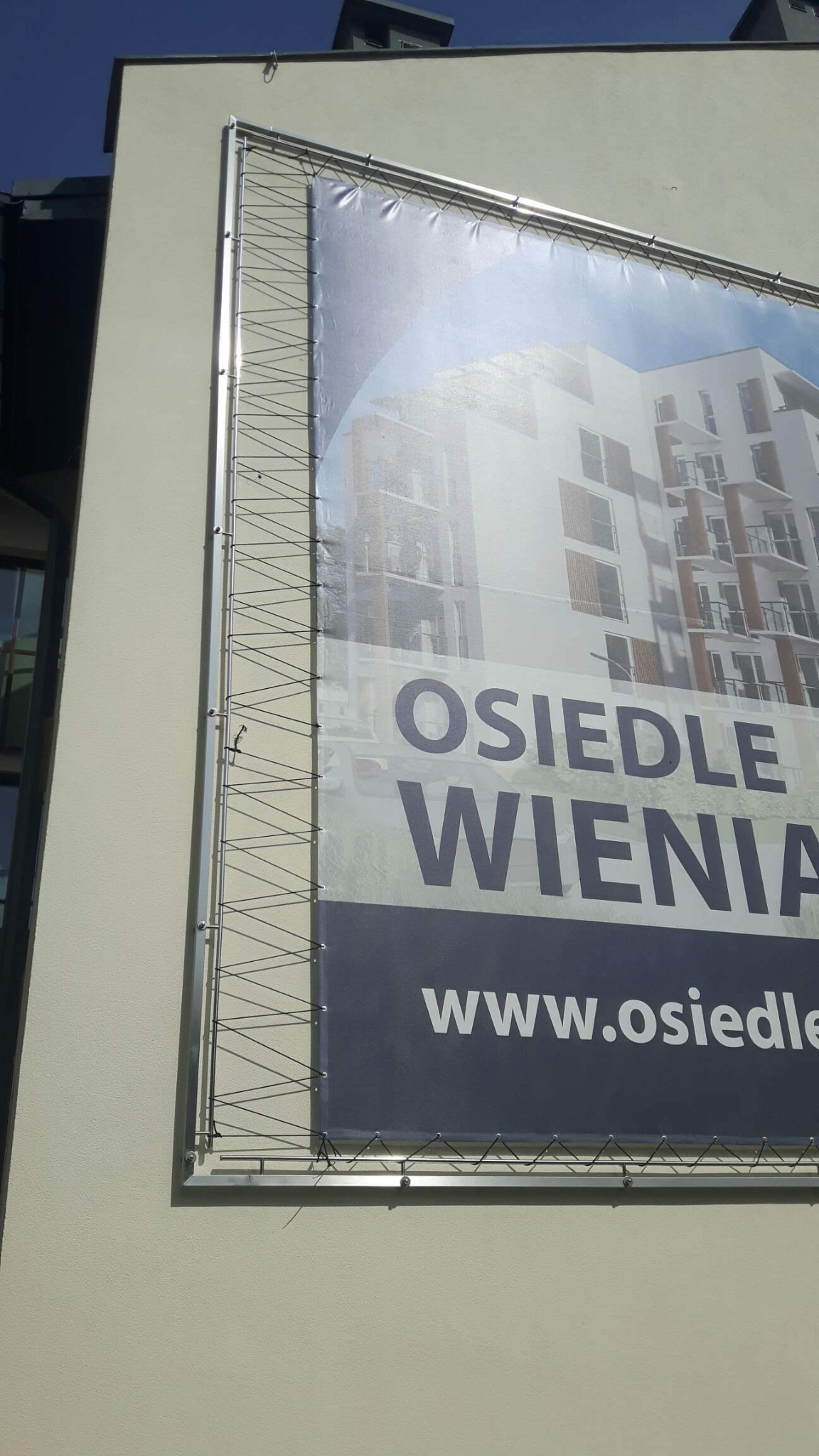 Baner reklamowy z konstrukcją nośną, prezentujący wizualizację osiedla mieszkaniowego na elewacji budynku.