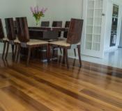 Błyszcząca, drewniana podłoga z egzotycznego drewna w jadalni z ciemnym stołem i krzesłami. W tle białe drzwi i bukiet kwiatów.