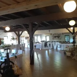 Sala bankietowa z dekoracjami ślubnymi: stoły z białymi obrusami, kwiatowe kompozycje, drewniane elementy dekoracyjne i podświetlane litery 'LOVE'.