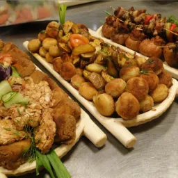 Dekoracyjne drewniane tace z różnorodnymi przekąskami: kotlety, ziemniaki pieczone i smażone, szaszłyki z warzywami i mięsem.