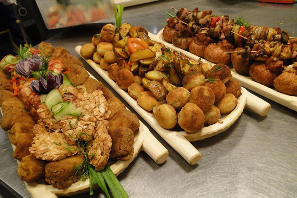 Dekoracyjne drewniane tace z różnorodnymi przekąskami: kotlety, ziemniaki pieczone i smażone, szaszłyki z warzywami i mięsem.